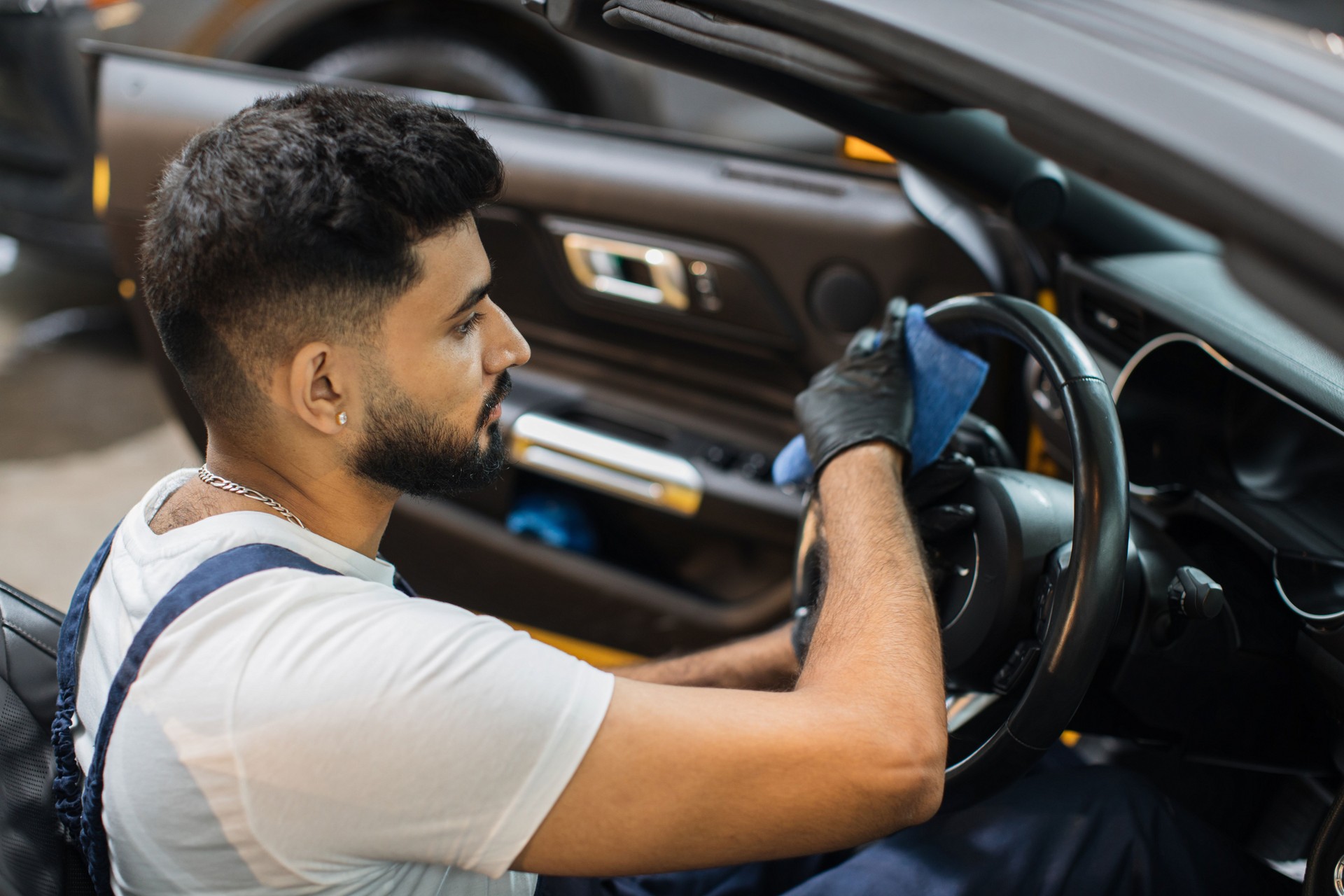 Handsome bearded young man in uniform and protective gloves, cleaning car interior