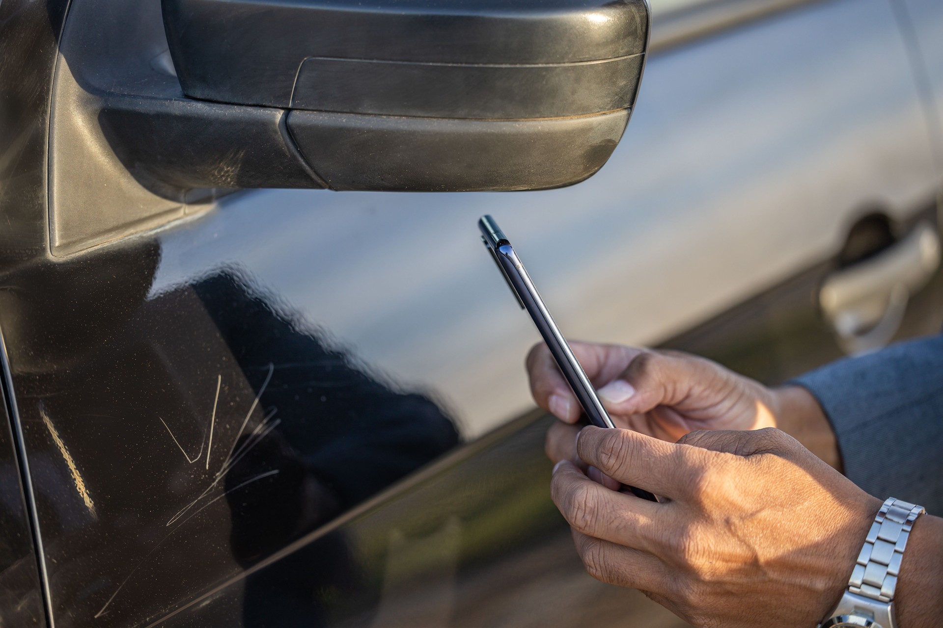 Detail of hands of insurance agent taking a picture of a car with a scratch.